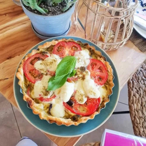 Tarte Soleil au Pesto et Mozzarella garnie de basilic frais sur une table.